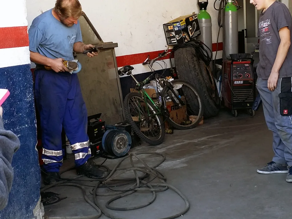 Zwei Personen arbeiten in einer Kfz-Werkstatt an Geräten.